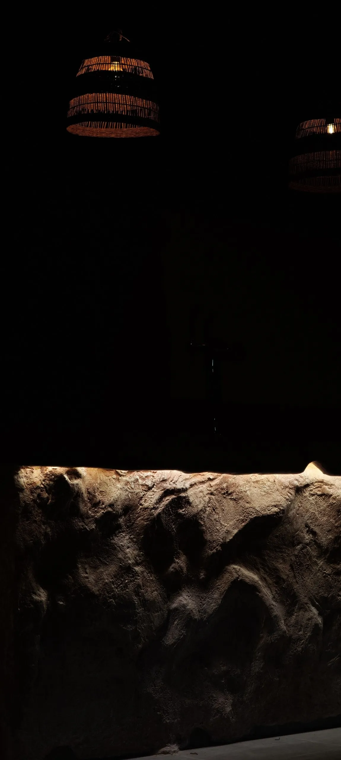 Woven pendant lamps above the sculpted stone bar counter in low light, Shidrah Studio