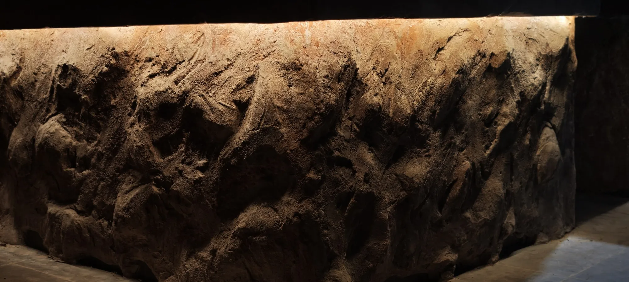 Full face of the hand-sculpted stone bar counter lit from the top edge, Shidrah Studio