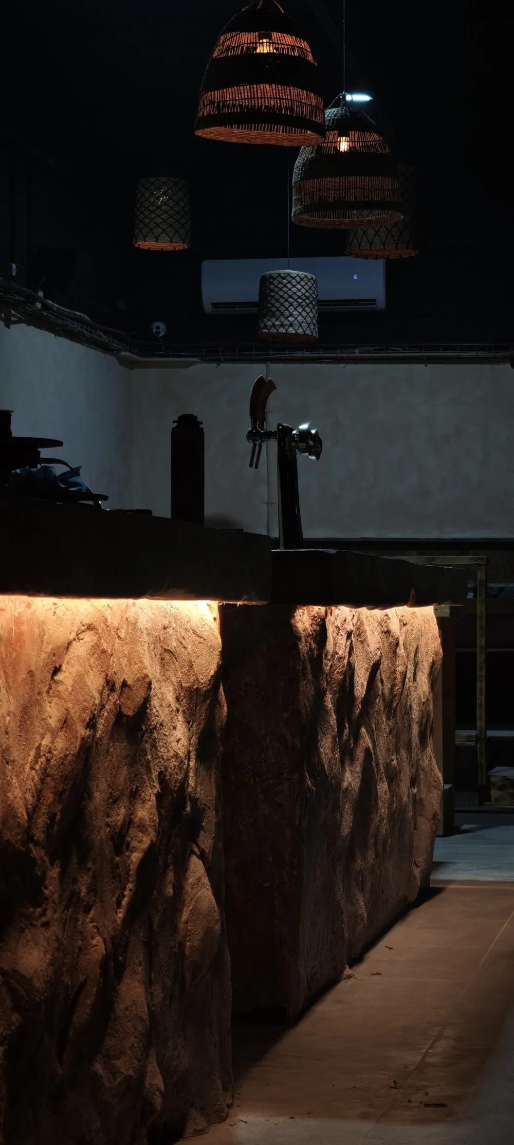 Hand-sculpted stone bar counter with under-lighting and woven pendant lamps, Shidrah Studio