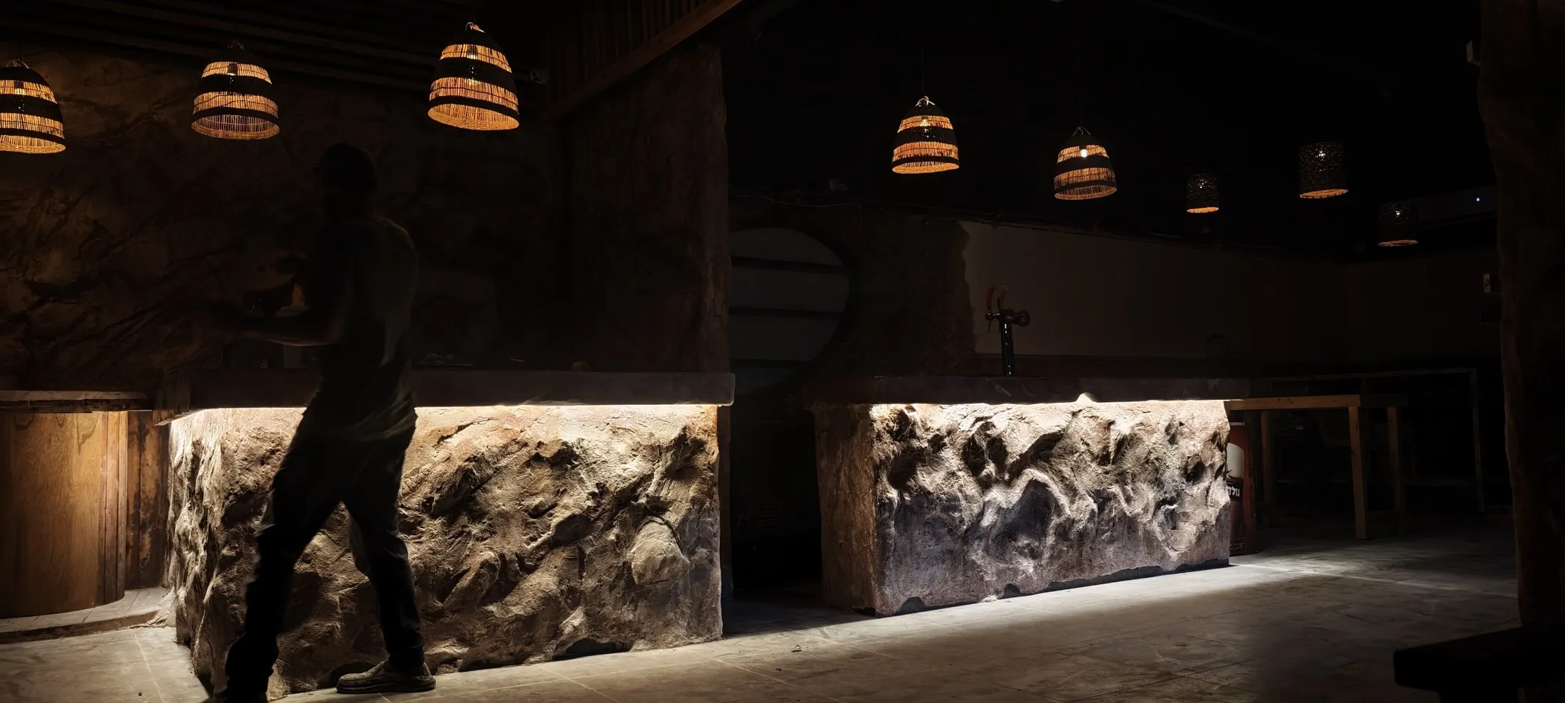The stone bar room, two hand-sculpted counters lit from beneath under woven pendant lamps, Shidrah Studio